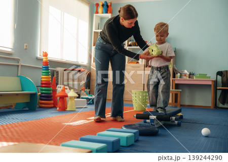 Doing balance training exercises. Preschool child with teacher during developmental activities in a playroom 139244290