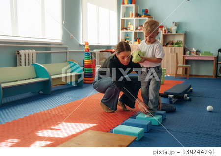 Doing balance training exercises. Preschool child with teacher during developmental activities in a playroom Doing balance training exercises. Preschool child with teacher during developmental activities in a playroom 139244291