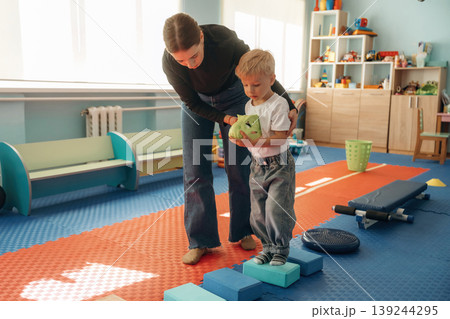 Path with cubes, balance training. Preschool child with teacher during developmental activities in a playroom Path with cubes, balance training. Preschool child with teacher during developmental activities in a playroom 139244295