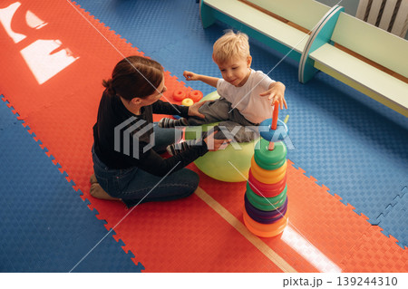 The balancing tricks on the ball. Preschool child with teacher during developmental activities in a playroom The balancing tricks on the ball. Preschool child with teacher during developmental activities in a playroom 139244310