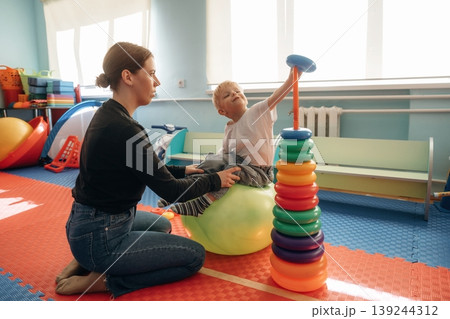 The balancing tricks on the ball. Preschool child with teacher during developmental activities in a playroom 139244312