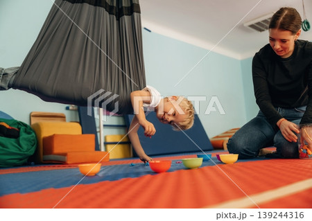 Putting the objects into bowls while hanging. Preschool child with teacher during developmental activities in a playroom 139244316