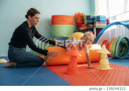 Exercises for motor skills. Preschool child with teacher during developmental activities in a playroom Exercises for motor skills. Preschool child with teacher during developmental activities in a playroom 139244322