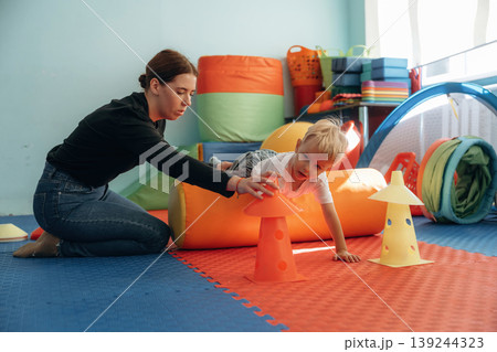 Exercises for motor skills. Preschool child with teacher during developmental activities in a playroom Exercises for motor skills. Preschool child with teacher during developmental activities in a playroom 139244323