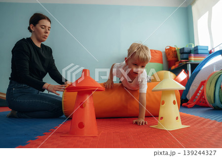 Control of the balance. Doing exercises. Preschool child with teacher during developmental activities in a playroom Control of the balance. Doing exercises. Preschool child with teacher during developmental activities in a playroom 139244327
