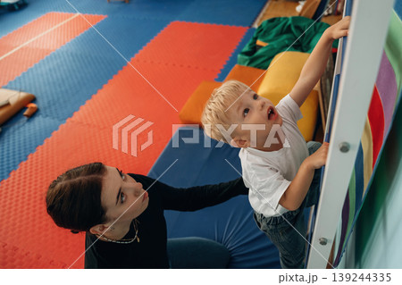 Climbing the ladder that is on the wall. Preschool child with teacher during developmental activities in a playroom 139244335