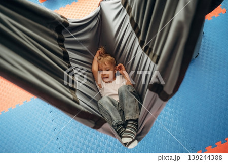 Lying down in the hammock. Cute preschool child, boy, during developmental activities in a playroom Lying down in the hammock. Cute preschool child, boy, during developmental activities in a playroom 139244388