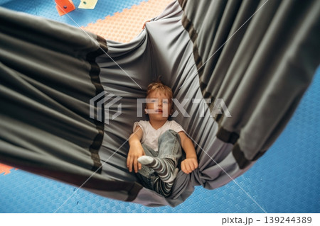 Lying down in the hammock. Cute preschool child, boy, during developmental activities in a playroom Lying down in the hammock. Cute preschool child, boy, during developmental activities in a playroom 139244389