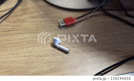Modern Wireless Earbud on a Wooden Desk with Charging Cable Modern Wireless Earbud on a Wooden Desk with Charging Cable 139244938