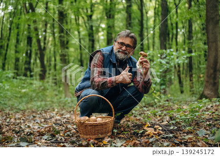 Positive facial expression, smiling. Mushroom picking. Man is in the forest at daytime 139245172