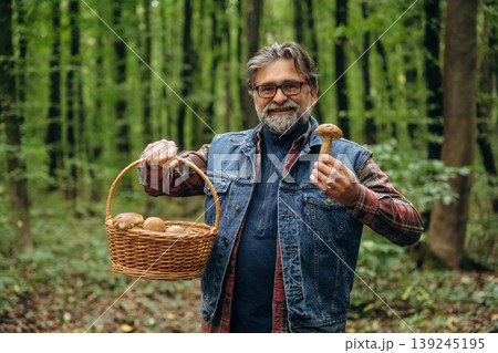 Looking at the camera. Mushroom picking. Man is in the forest at daytime Looking at the camera. Mushroom picking. Man is in the forest at daytime 139245195