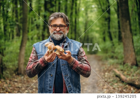 Raw food is in hands. Mushroom picking. Man is in the forest at daytime Raw food is in hands. Mushroom picking. Man is in the forest at daytime 139245205