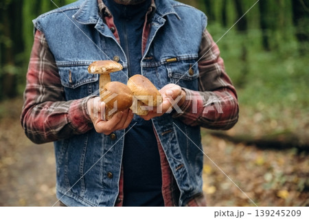 Showing mushrooms, holding them in hands. Close up view of is standing in the forest 139245209