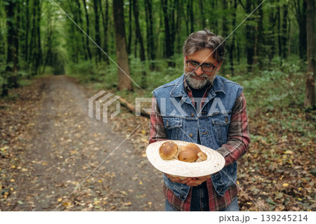 In the hat, holding in hands. Mushroom picking. Man is in the forest at daytime In the hat, holding in hands. Mushroom picking. Man is in the forest at daytime 139245214