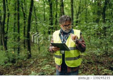 Quality control, with notepad. Senior forest ecologist is working in the woods. In the uniform Quality control, with notepad. Senior forest ecologist is working in the woods. In the uniform 139245235