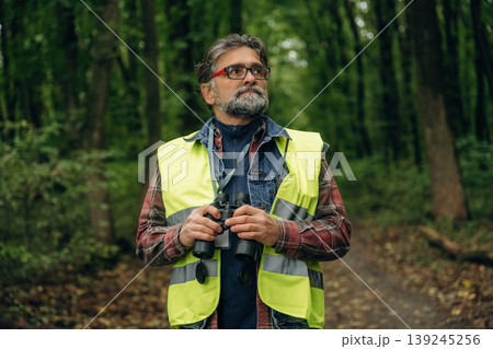 Professional binoculars in hands. Senior forest ecologist is working in the woods. In the uniform Professional binoculars in hands. Senior forest ecologist is working in the woods. In the uniform 139245256