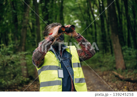 Professional binoculars in hands. Senior forest ecologist is working in the woods. In the uniform Professional binoculars in hands. Senior forest ecologist is working in the woods. In the uniform 139245258