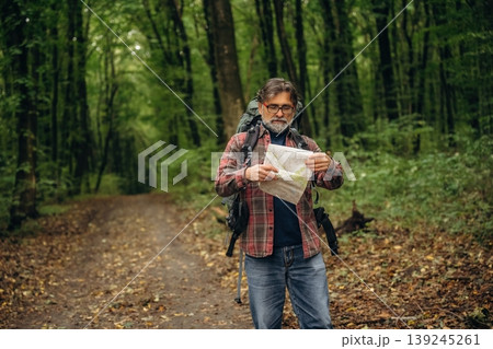 Paper map is in hands. Hiking experience, senior man is in the forest at daytime Paper map is in hands. Hiking experience, senior man is in the forest at daytime 139245261