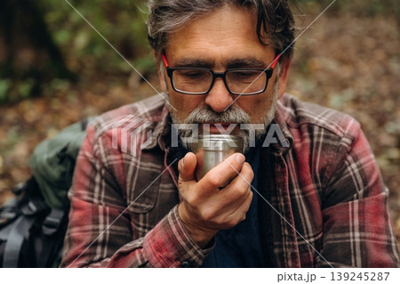 Warm drink in hands, thermos. Hiking experience, senior man is in the forest at daytime 139245287