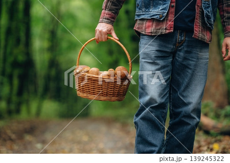Standing with basket in hand. Close up view of man that is doing mushroom picking in the forest 139245322