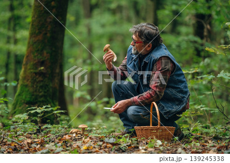 Identification if it's safe one. Mushroom picking. Man is in the forest at daytime Identification if it's safe one. Mushroom picking. Man is in the forest at daytime 139245338