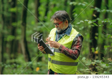 Gathering information, reading from notepad. Senior forest ecologist is working in the woods. In the uniform Gathering information, reading from notepad. Senior forest ecologist is working in the woods. In the uniform 139245343