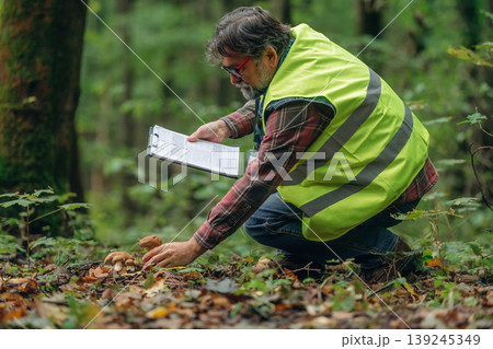 Safe to eat or not, checking, with notepad. Senior forest ecologist is working in the woods. In the uniform Safe to eat or not, checking, with notepad. Senior forest ecologist is working in the woods. In the uniform 139245349