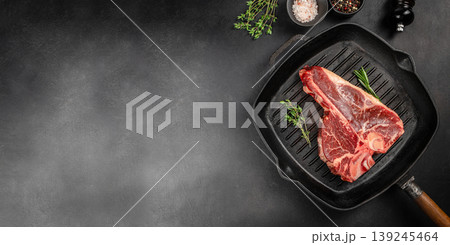 Raw porterhouse t-bone steak on grill pan with herbs and spices on dark background with copy space for bbq advertising Raw porterhouse t-bone steak on grill pan with herbs and spices on dark background with copy space for bbq advertising 139245464