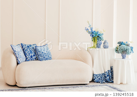 Elegant beige sofa with blue pillows and floral decor in bright living room interior with copy space 139245518