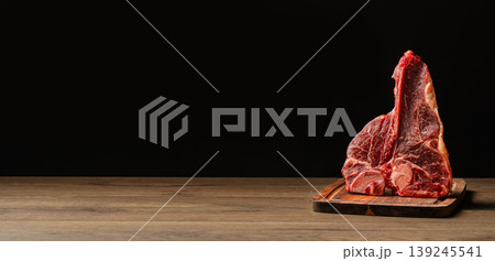 Raw t-bone steak standing on wooden board, dark background with copy space Raw t-bone steak standing on wooden board, dark background with copy space 139245541