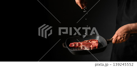 Chef seasoning raw steak with salt over grill pan on black background. copy space Chef seasoning raw steak with salt over grill pan on black background. copy space 139245552