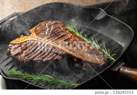 Grilled t-bone steak with rosemary on cast iron pan, smoky hot surface Grilled t-bone steak with rosemary on cast iron pan, smoky hot surface 139245553