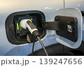 White electric vehicle charging port close-up with plugged charger connector and open charge door 139247656