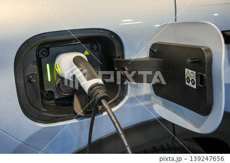 White electric vehicle charging port close-up with plugged charger connector and open charge door 139247656