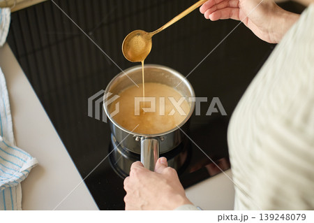 Person lifts thick sauce with spoon above saucepan on cooktop. Concept of home cooking Person lifts thick sauce with spoon above saucepan on cooktop. Concept of home cooking 139248079