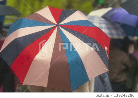Close-up of Rainbow Umbrella in Rain. Colorful bright umbrella with raindrops fills frame among blurred umbrellas during rainy outdoor crowd scene. Concept of umbrella protection, season weather Close-up of Rainbow Umbrella in Rain. Colorful bright umbrella with raindrops fills frame among blurred umbrellas during rainy outdoor crowd scene. Concept of umbrella protection, season weather 139248286