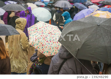 Crowd gathers with umbrellas during rain at public event outdoors, showing people in jackets and hoods among umbrellas. Concept of crowd, weather, gathering, protection, city life, travel, event Crowd gathers with umbrellas during rain at public event outdoors, showing people in jackets and hoods among umbrellas. Concept of crowd, weather, gathering, protection, city life, travel, event 139248290