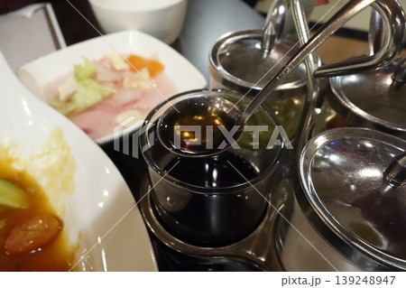Sauce Spoon Over Condiment Containers in Restaurant Setting 139248947