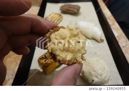 Hand Holding Nuts-Topped Pastry with Assorted Baked Goods Hand Holding Nuts-Topped Pastry with Assorted Baked Goods 139248955