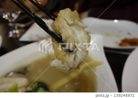 Chopsticks Holding Steamed Dumpling Over Soup Dish 139248972