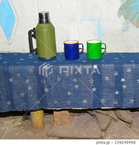 green thermos and two mugs stand on a long bench covered with blue fabric with stars 139249498