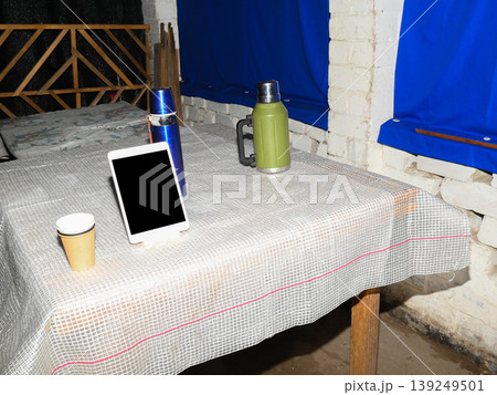 two thermoses of different colors and a modern tablet on a table with a white protective tablecloth two thermoses of different colors and a modern tablet on a table with a white protective tablecloth 139249501