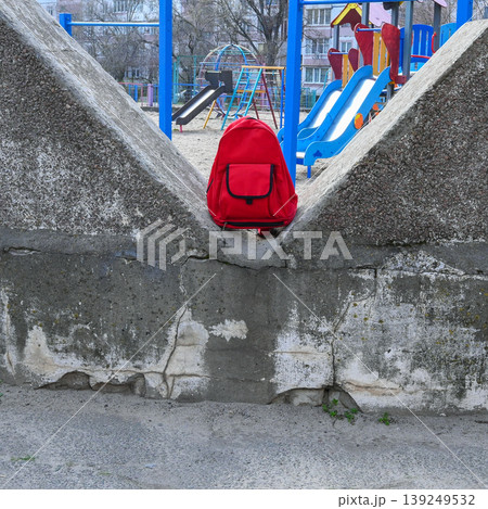red backpack stands in a recess of a concrete wall against the background of a bright playground red backpack stands in a recess of a concrete wall against the background of a bright playground 139249532