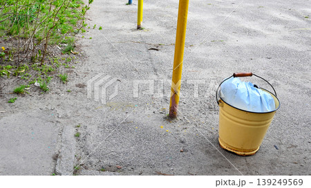 yellow bucket with blue bag on asphalt near poles 139249569
