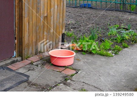 pink plastic basin stands on a concrete path in the garden against a wooden shed and beds pink plastic basin stands on a concrete path in the garden against a wooden shed and beds 139249580