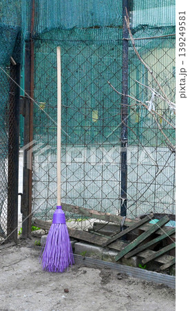 new broom with purple pile on a long wooden handle stands by a mesh fence in the garden new broom with purple pile on a long wooden handle stands by a mesh fence in the garden 139249581