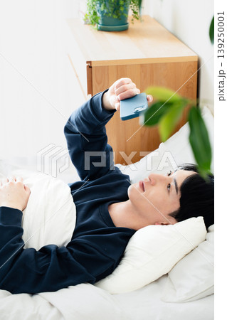 ベッドでスマホを見る若い男性 139250001