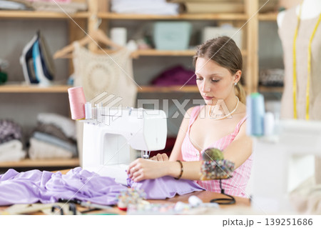 Young seamstress sews a dress on a machine Young seamstress sews a dress on a machine 139251686