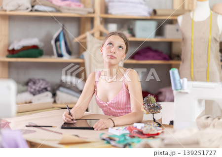 woman stands with a tablet in her hands in a sewing workshop woman stands with a tablet in her hands in a sewing workshop 139251727