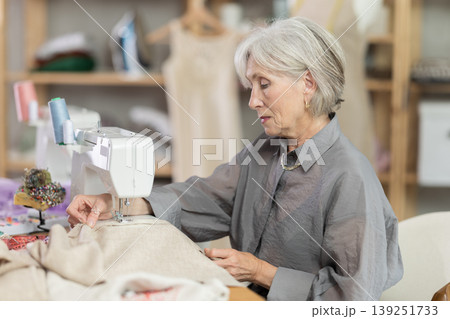Woman seamstress sews on sewing machine in workshop Woman seamstress sews on sewing machine in workshop 139251733